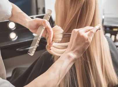 Coiffeur coupant les longs cheveux blonds d'une cliente avec des ciseaux et un peigne à Valence dans le Tarn-et-Garonne 82