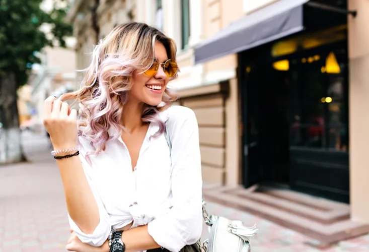 Jeune femme blonde souriante, lunettes de soleil, chemise blanche, et un sac sur une rue de la ville à Valence dans le Tarn-et-Garonne 82